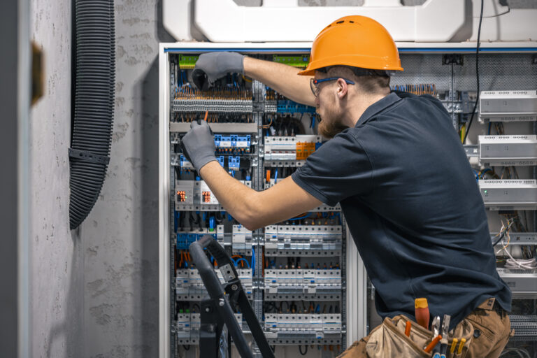 Male electrician working in a switchboard with fuses. Installation and connection of electrical equipment. Professional with tools in hand.